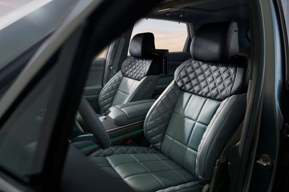 Quilted leather front seats of a Genesis GV80 hybrid SUV viewed through the open door, showing two-tone grey and black upholstery with diamond stitching and a centre console between them