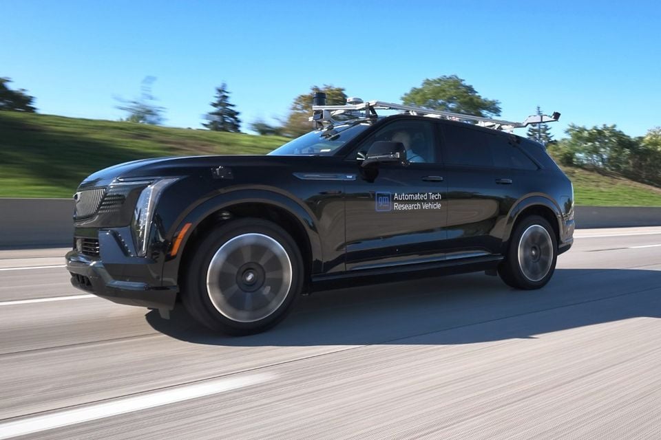 Um Cadillac Escalade IQ SUV preto equipado como um veículo de pesquisa de tecnologia automatizado da GM com sensores montados no teto, dirigindo em uma rodovia