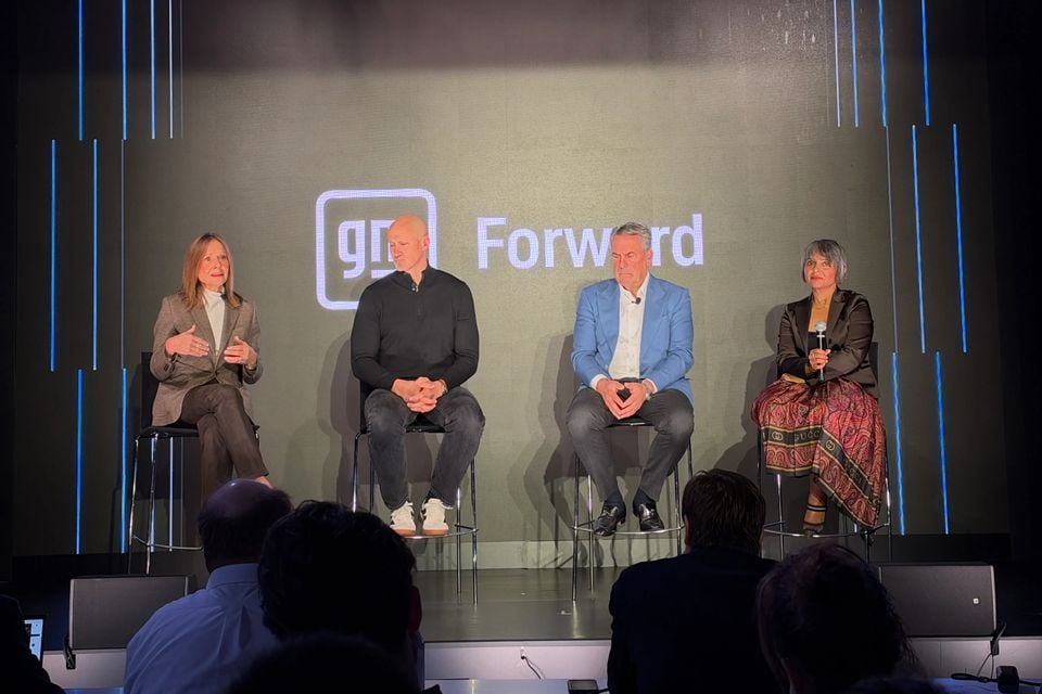 Four panellists seated on stage in front of a GM Forward screen, with a woman on the left speaking to an audience