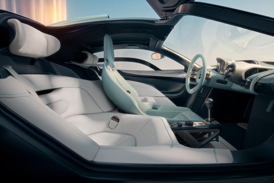 Interior of the Gordon Murray S1 showing white leather bucket seats, a minimalist dashboard, circular steering wheel, carbon fibre centre console and gull-wing door open wide