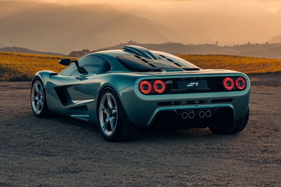 A teal Gordon Murray S1 supercar seen from the rear three-quarter angle at sunset, showing circular tail lights and quad exhaust tips