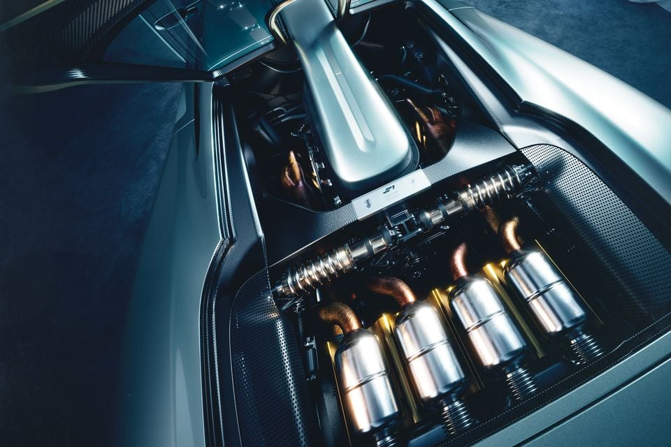 The mid-mounted engine bay of the Gordon Murray S1 supercar, showing polished exhaust headers and intake components in a carbon fibre enclosure