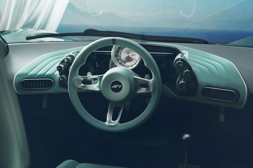 Interior of the Gordon Murray S1 showing a retro-styled mint green dashboard, circular analogue gauge, digital instrument display, and three-spoke steering wheel with S1 badging