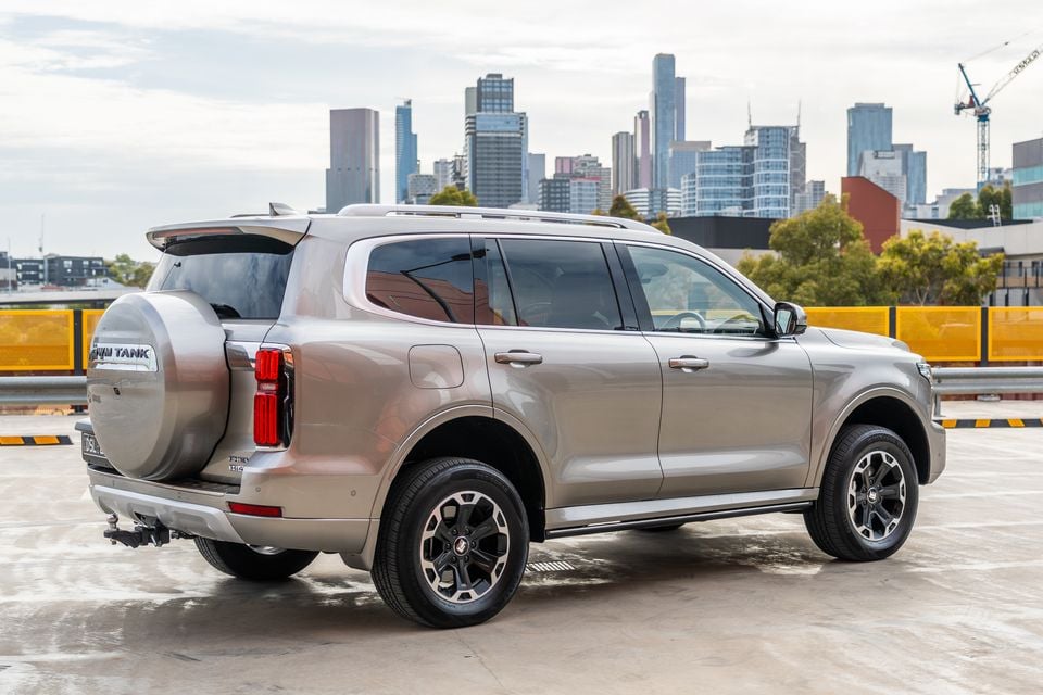 A GWM Tank 500 Hi4-T PHEV large SUV seen from the rear three-quarter angle on a rooftop car park with a city skyline in the background