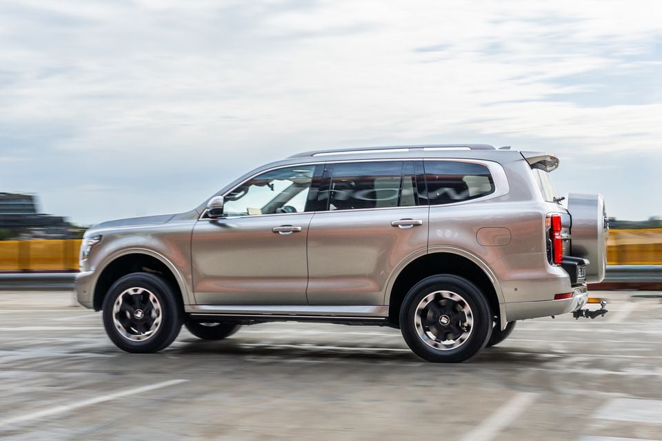 A gold/beige GWM Tank 500 large SUV seen from the side while driving, with a spare wheel mounted on the rear