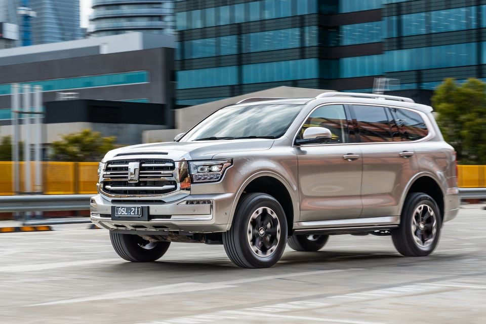 A gold/champagne GWM Tank 500 large SUV seen from the front-side while driving through an urban area