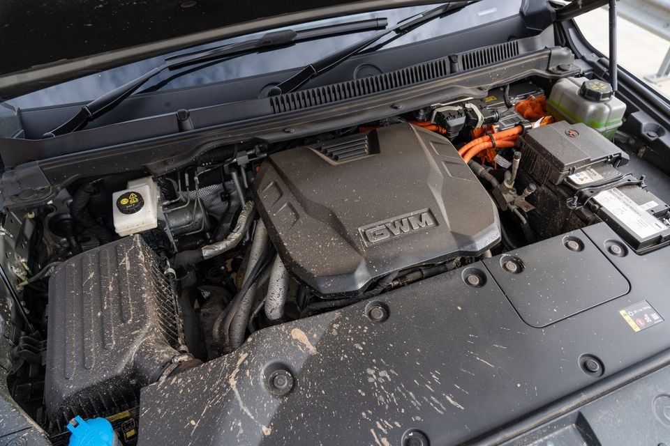 GWM Tank 500 PHEV engine bay showing the GWM-branded engine cover with orange high-voltage cables indicating hybrid powertrain components, covered in mud splatter