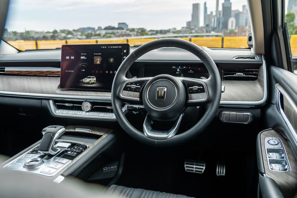 Interior of a GWM Tank 500 PHEV showing the steering wheel, large touchscreen infotainment display, digital instrument cluster, centre console, and timber-trimmed dashboard