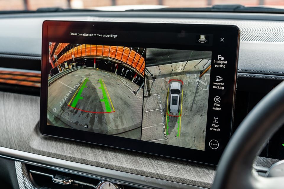 The infotainment touchscreen inside a GWM Tank 500 Hi4-T PHEV showing a split-screen reversing camera view with bird's-eye surround-view and rear camera feed, with parking guidelines displayed in a car park.