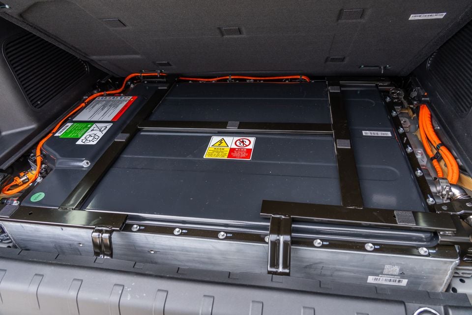 The high-voltage battery pack of a GWM Tank 500 Hi4-T PHEV, visible under the boot floor with orange high-voltage cables and warning labels.