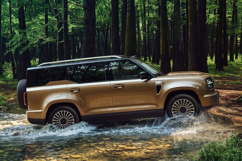 A gold Haval H10 large SUV seen from the side, fording a shallow creek in a forest setting