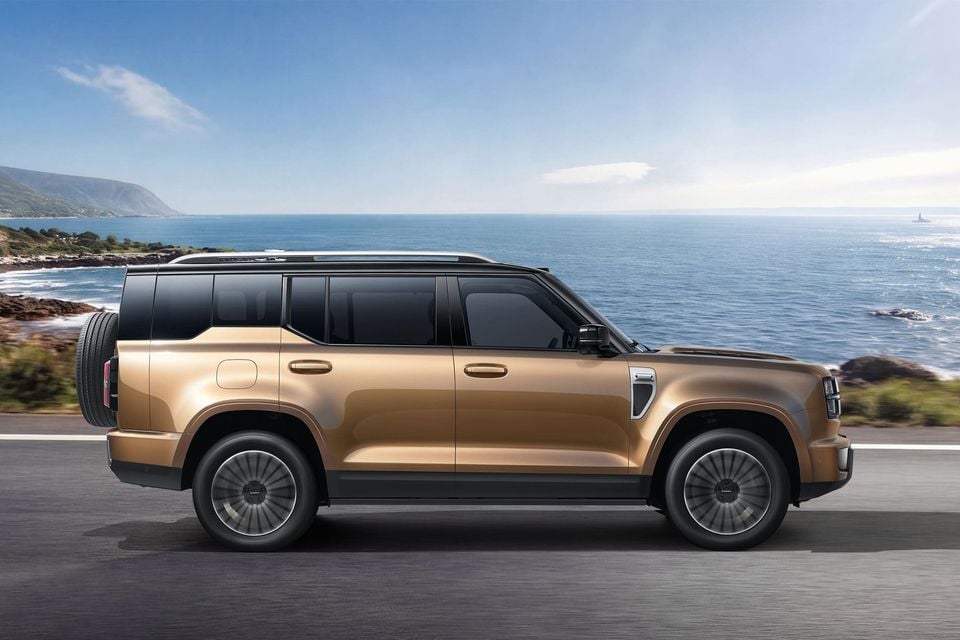 A gold Haval H10 large SUV seen from the side, driving along a coastal road with ocean views in the background