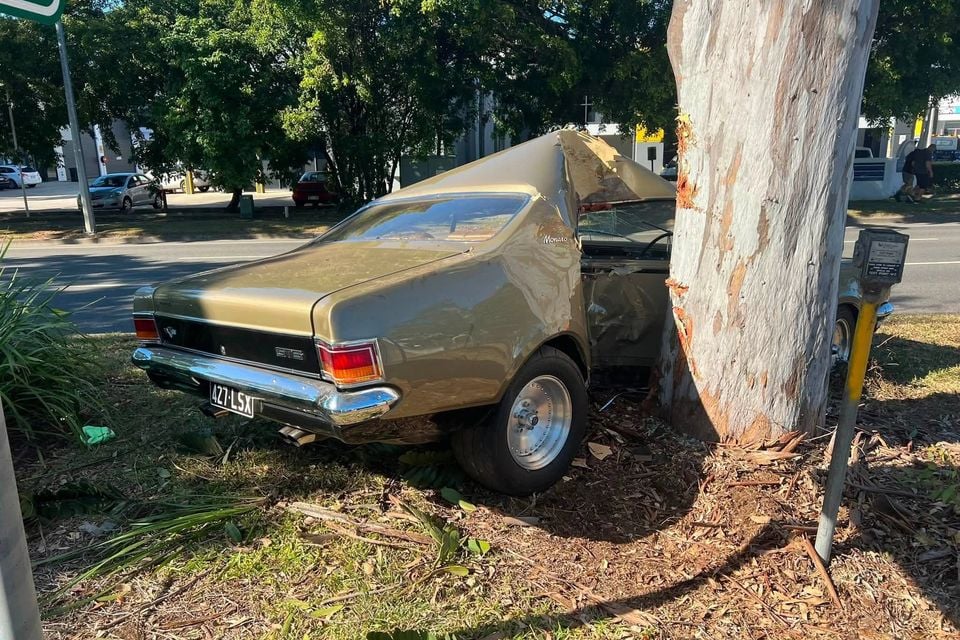 A gold Holden Monaro coupe with severe crash damage to its passenger side after colliding with a large tree on a suburban street in Queensland.