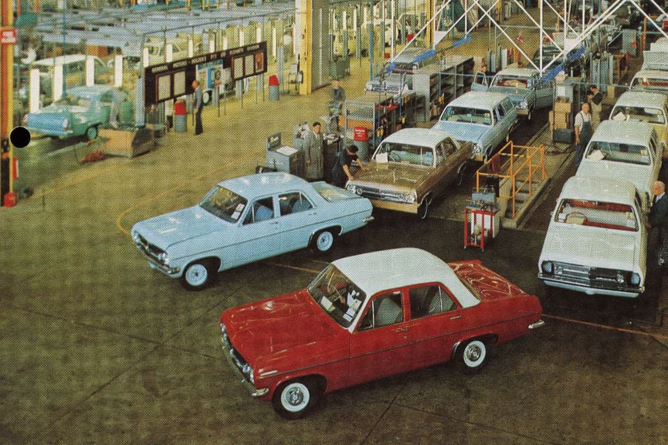 Vintage photograph of Holden vehicles on an assembly line at the Elizabeth manufacturing plant in South Australia, showing multiple sedans including a red and a light blue Holden being assembled by workers