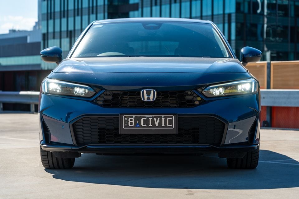 A dark blue Honda Civic e:HEV seen from the front, parked on a rooftop car park with a city building in the background.