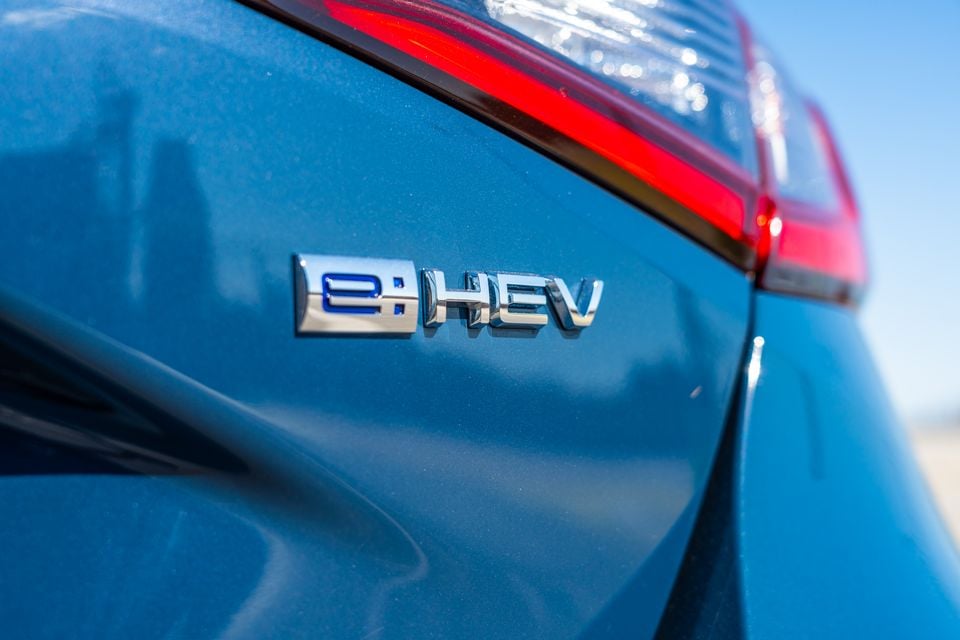 Close-up of the e:HEV hybrid badge on the rear of a blue Honda Civic, with a tail light visible in the background.