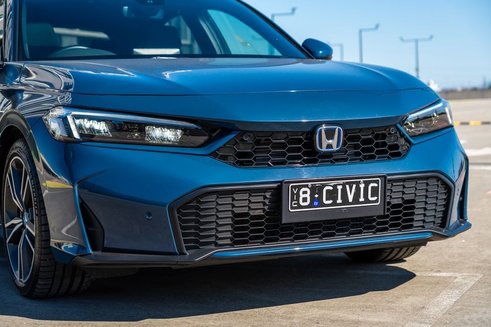 Close-up of the front grille and headlights of a blue Honda Civic e:HEV, showing the Honda badge and a Victorian number plate reading '8 CIVIC'.