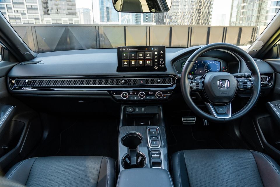 Interior view of a Honda Civic e:HEV showing the dashboard, touchscreen infotainment system, steering wheel, centre console and climate controls, with a right-hand drive layout