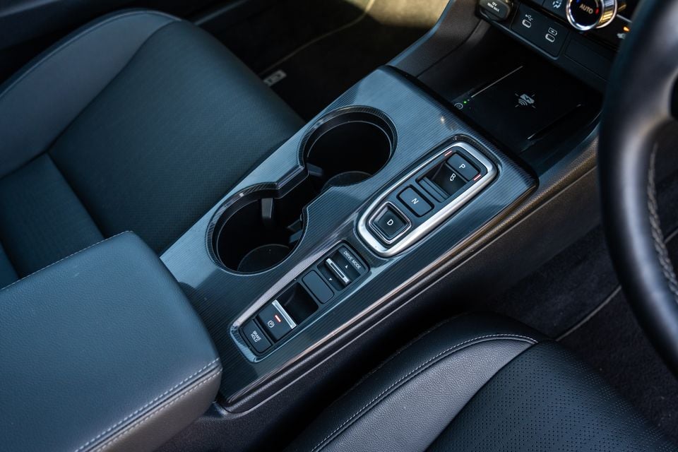 Interior centre console of a Honda Civic e:HEV showing electronic gear selector buttons, drive mode controls, cup holders, and wireless charging pad