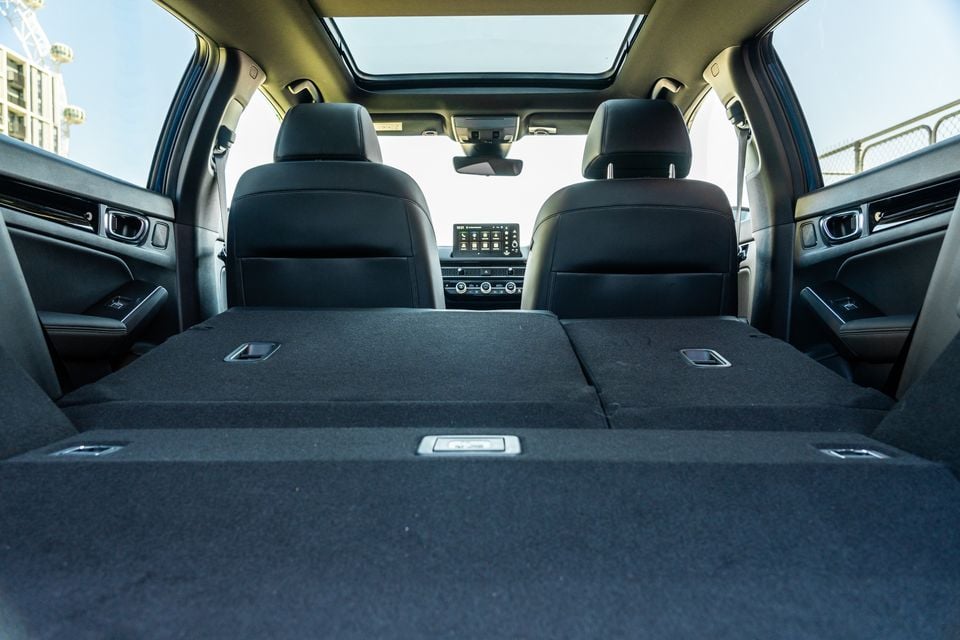 Interior cargo area of a Honda Civic e:HEV with rear seats folded flat, showing a large load floor, touchscreen infotainment system, and panoramic sunroof visible from the boot.