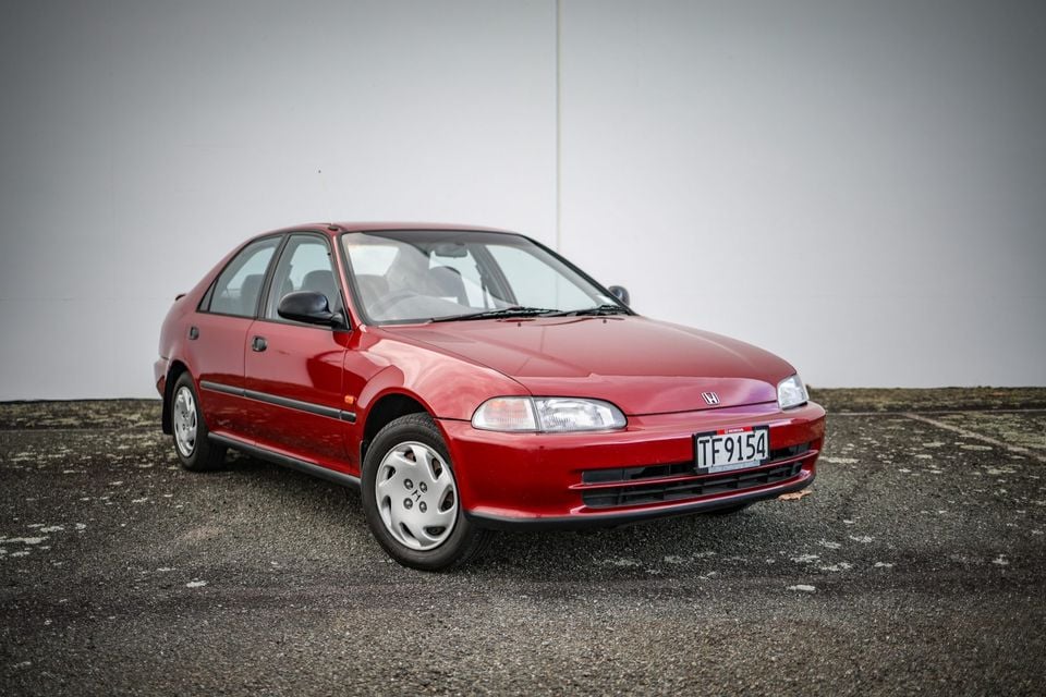 A red Honda Civic sedan parked in a car park, seen from the front-side angle