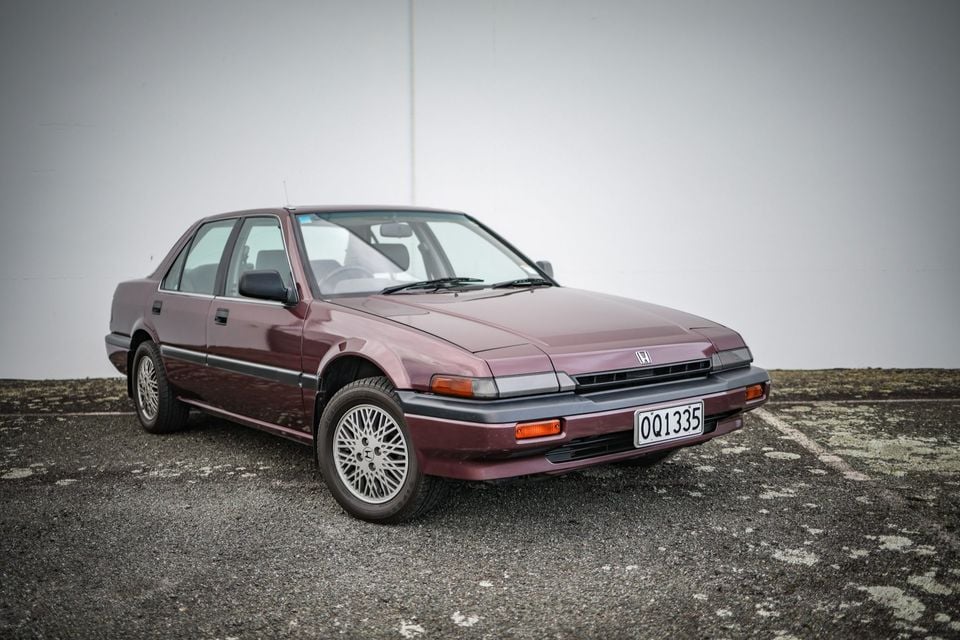 A maroon Honda Accord sedan from the late 1980s parked in an outdoor car park, seen from the front-left side