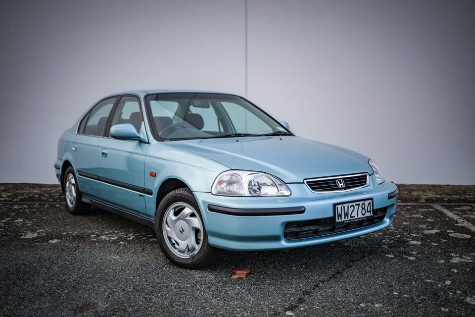 A light blue Honda Civic sedan parked on a concrete surface, seen from the front-side angle