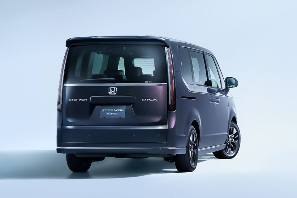 A dark purple Honda Step WGN Spada e:HEV minivan, seen from the rear at an angle, on a plain grey studio background.