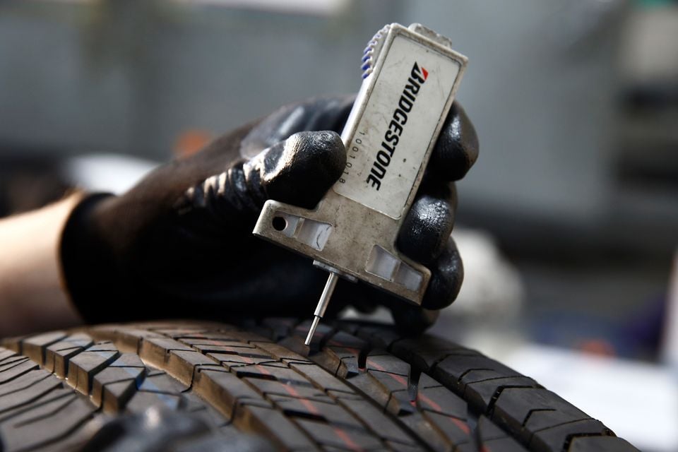 A gloved hand holds a Bridgestone tyre tread depth gauge against the tread of a car tyre