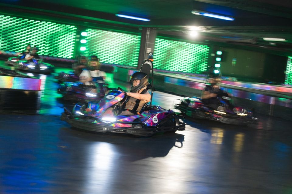 People racing colourful electric go-karts on an indoor karting track with neon green lighting