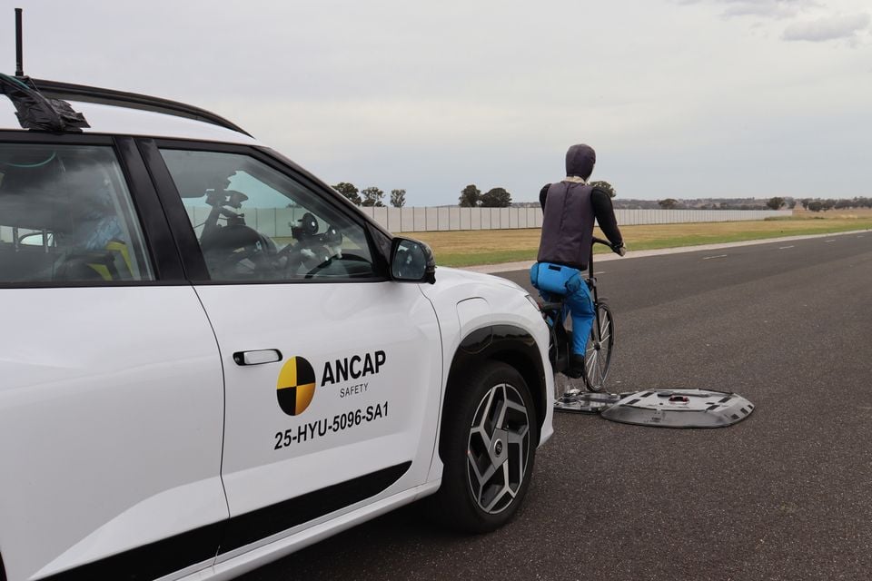 White Hyundai Elexio SUV with ANCAP Safety decals during an autonomous emergency braking test with a cyclist dummy target on a test track