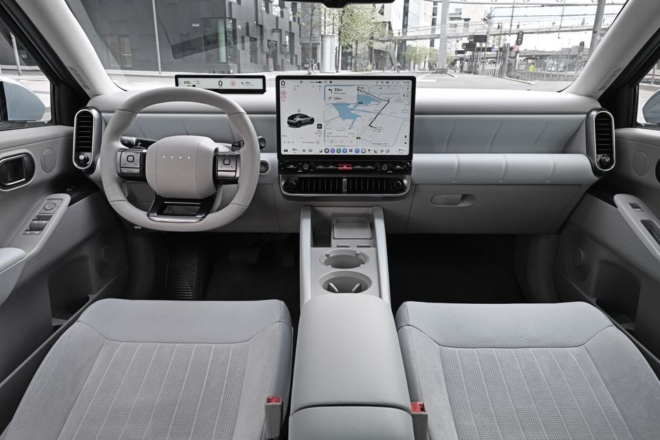 The interior of a Hyundai Ioniq, showing a light grey cabin with dual digital screens, a steering wheel, and front seats.