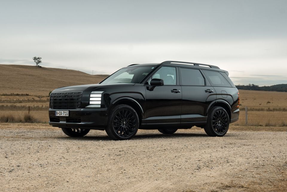 A black Hyundai Palisade large SUV seen from the front-side angle, parked on a gravel road in a rural landscape