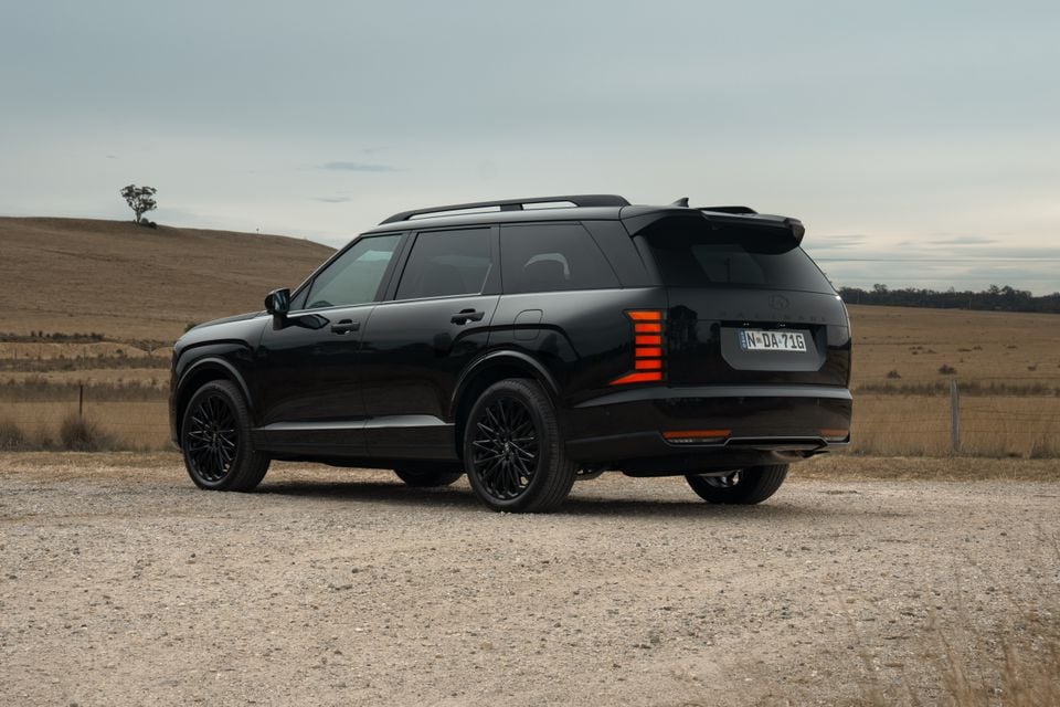 A black Hyundai Palisade Calligraphy large SUV seen from the rear three-quarter angle on a gravel road in a rural Australian setting