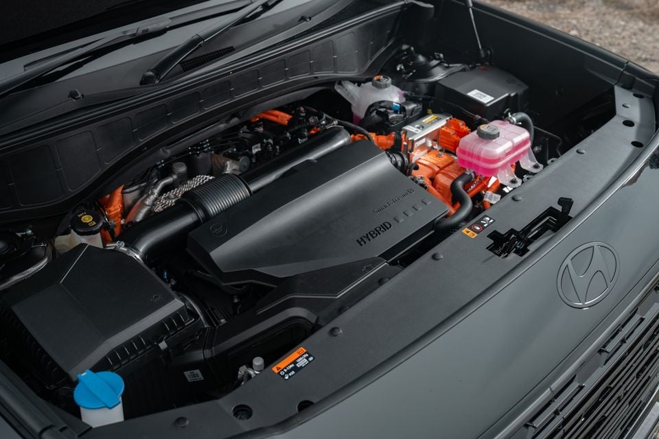 The hybrid engine bay of a Hyundai Palisade, showing the SmartStream hybrid powertrain with orange high-voltage components and the Hyundai logo on the strut brace