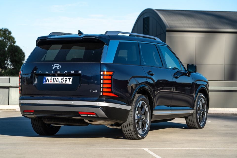 Rear three-quarter view of a dark blue Hyundai Palisade Hybrid SUV parked in a car park, showing the tailgate badging and tail lights