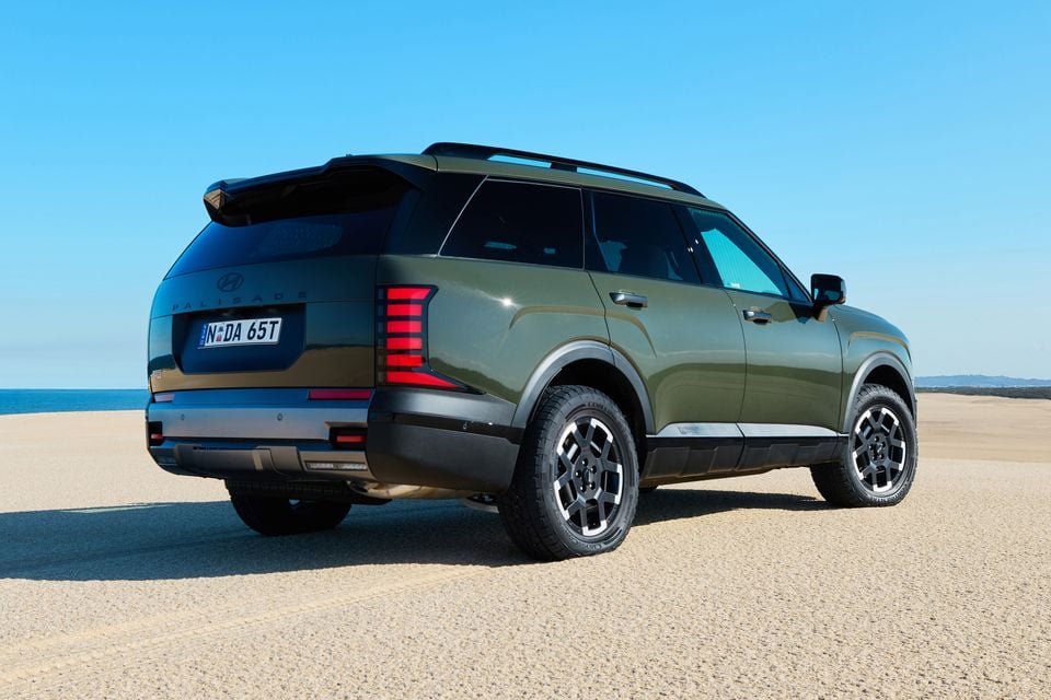 A green Hyundai Palisade XRT Pro large SUV seen from the rear three-quarter angle on a sandy beach setting