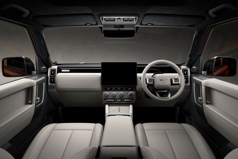 Interior view of a right-hand drive SUV cabin showing a light grey dashboard, large central touchscreen, round climate controls, and perforated leather front seats
