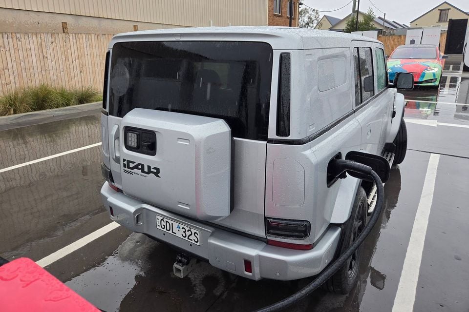 A silver iCar V25 electric SUV seen from the rear, plugged in to charge at a wet car park in Australia