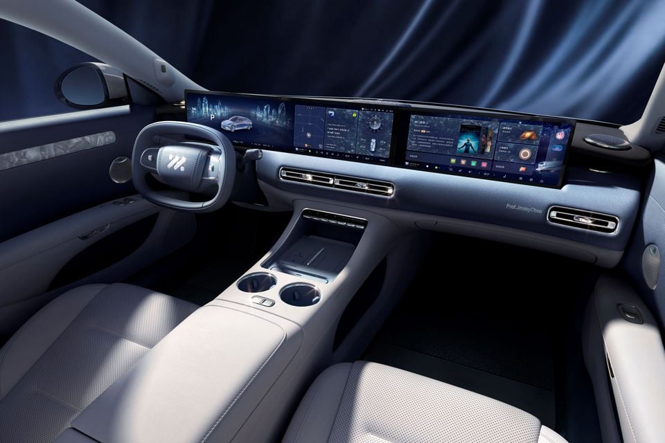 Interior of the IM Motors L6 or IM5 showing a wide panoramic touchscreen display spanning the dashboard, a flat-bottomed steering wheel, light grey upholstery, and a minimalist centre console with cup holders.
