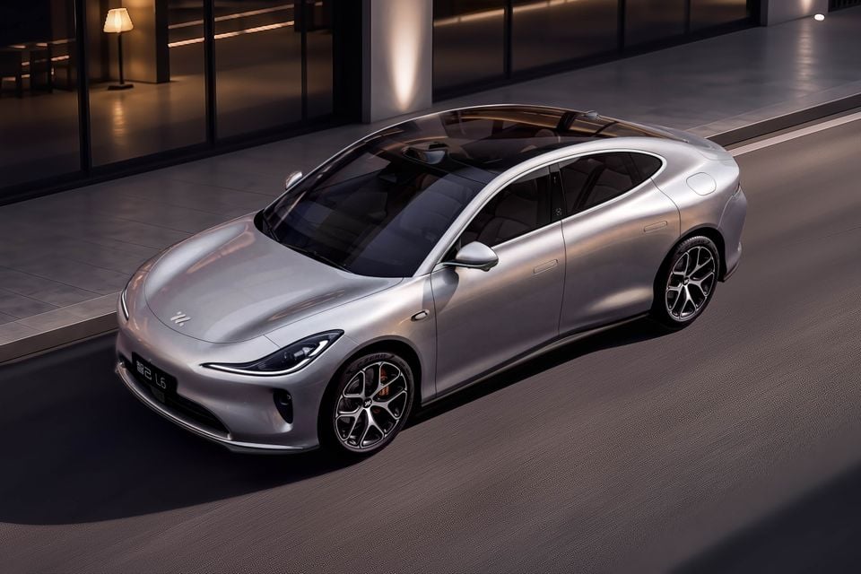 A silver IM L6 sedan seen from a elevated front-three-quarter angle, parked outside a modern building at night