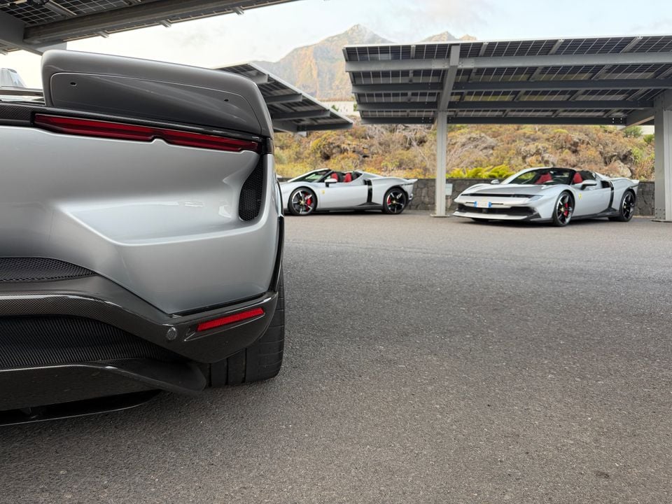 Three grey Ferrari supercars parked under a solar-panelled canopy with a mountain backdrop, seen from the rear of the closest car