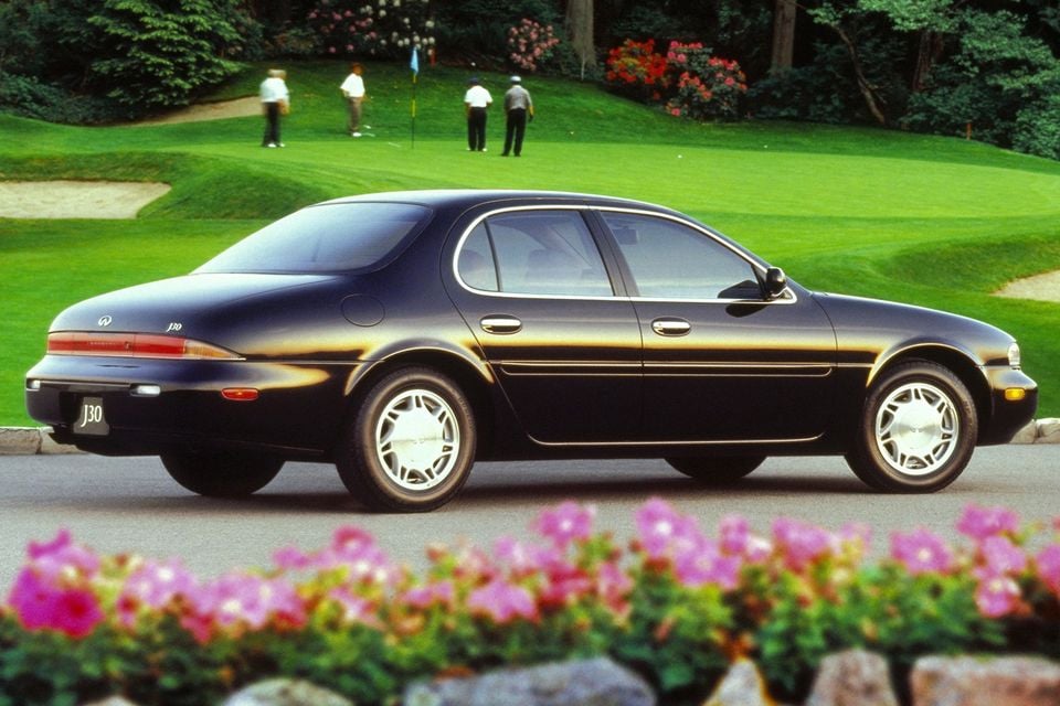 An Infiniti J30 sedan seen from the side, parked near a golf course with flowers in the foreground.