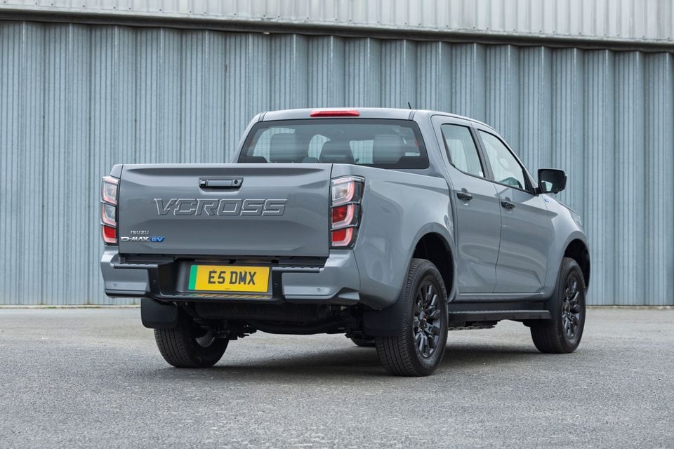 A grey Isuzu D-Max EV V-Cross dual-cab ute parked in front of a corrugated metal wall, seen from the rear quarter