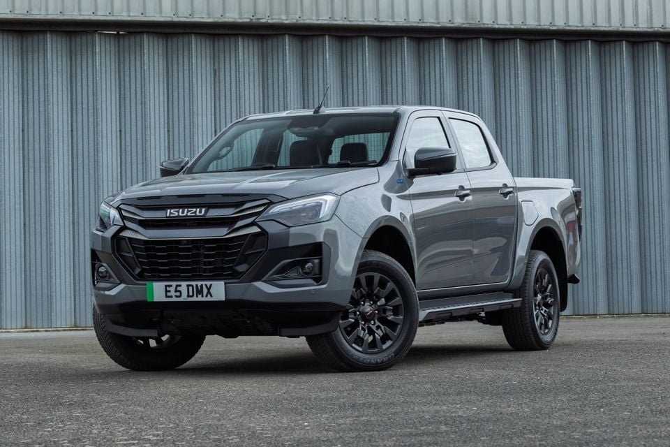 A grey Isuzu D-Max dual-cab ute parked in front of a metal warehouse wall, seen from the front quarter.
