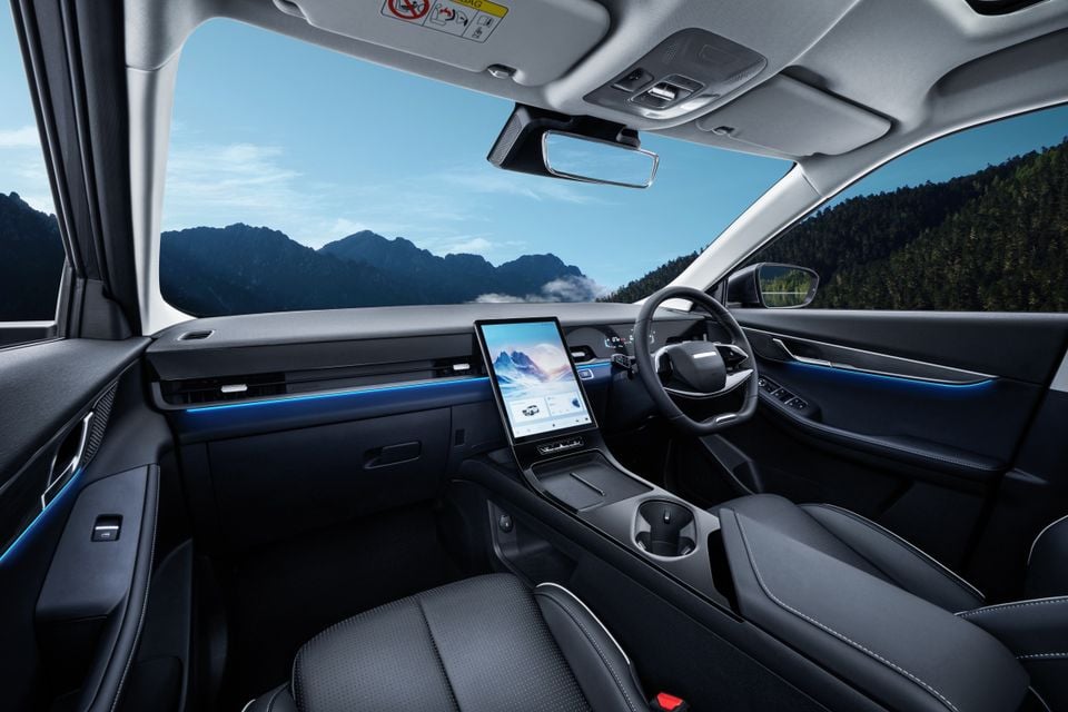 Interior of the Jaecoo J5 hybrid showing the dashboard, large central touchscreen infotainment display, steering wheel, and dark upholstery with blue ambient lighting
