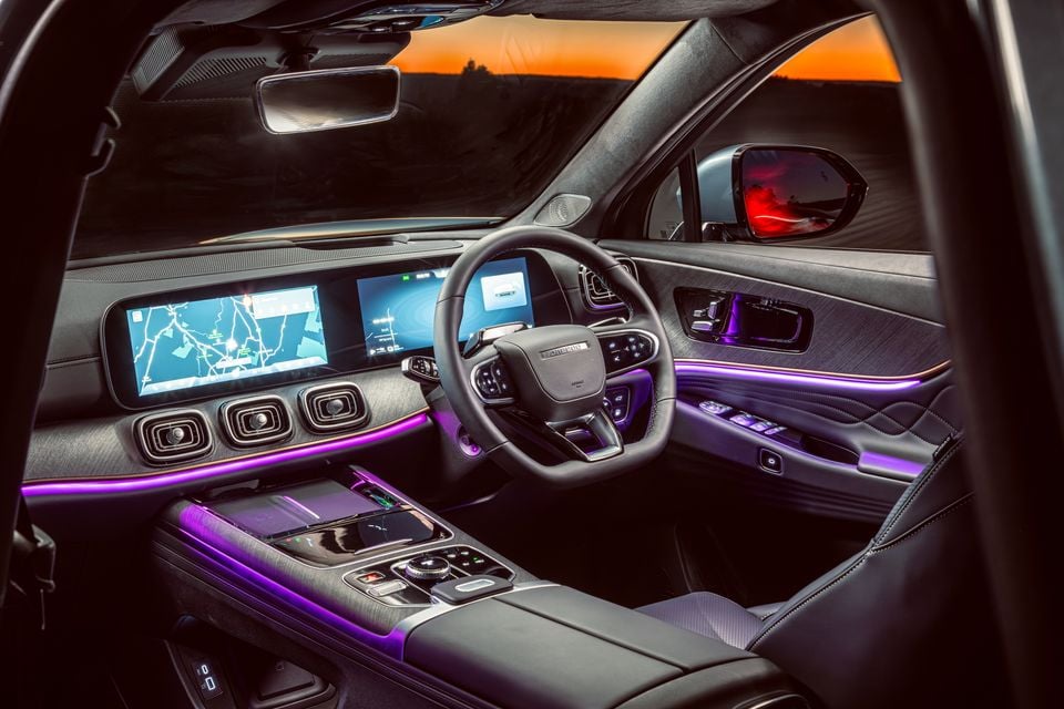 The interior of a Jaecoo J8 showing dual digital screens, a flat-bottomed steering wheel, and purple ambient lighting throughout the cabin at dusk