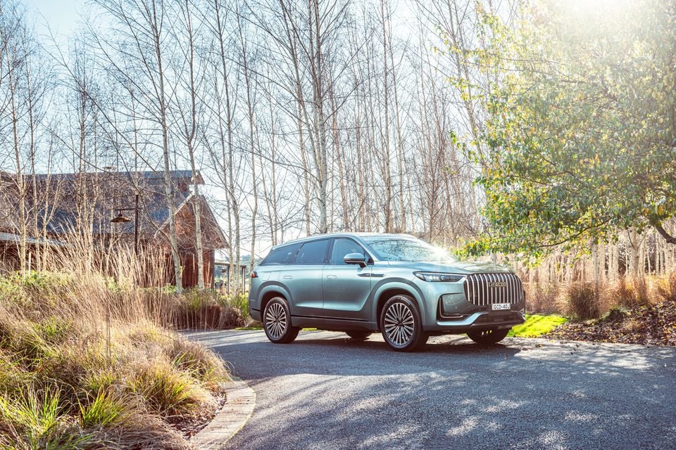 A teal Jaecoo J8 large SUV parked on a driveway surrounded by bare trees and autumn foliage