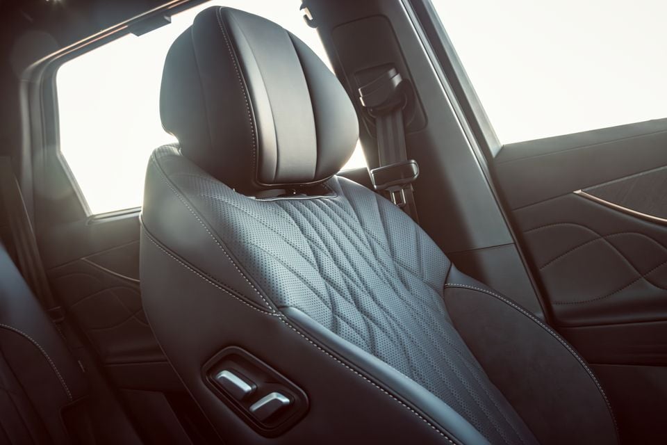 Close-up of the rear of a front seat in a car interior, showing quilted perforated leather upholstery, a headrest, seatbelt, and seat adjustment controls