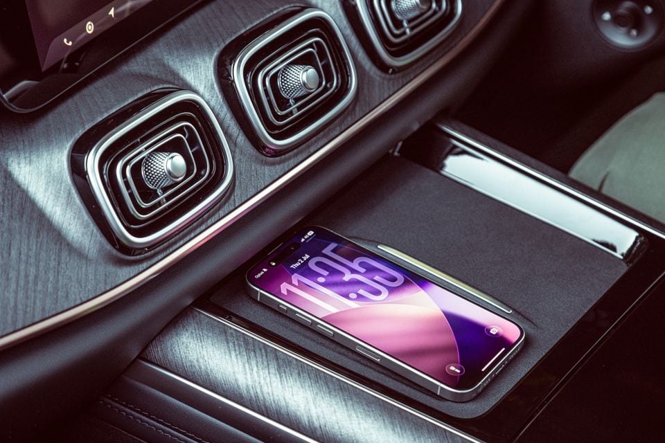 A smartphone resting on the wireless charging pad in the centre console of a Jaecoo J8, with stylised air vents visible above